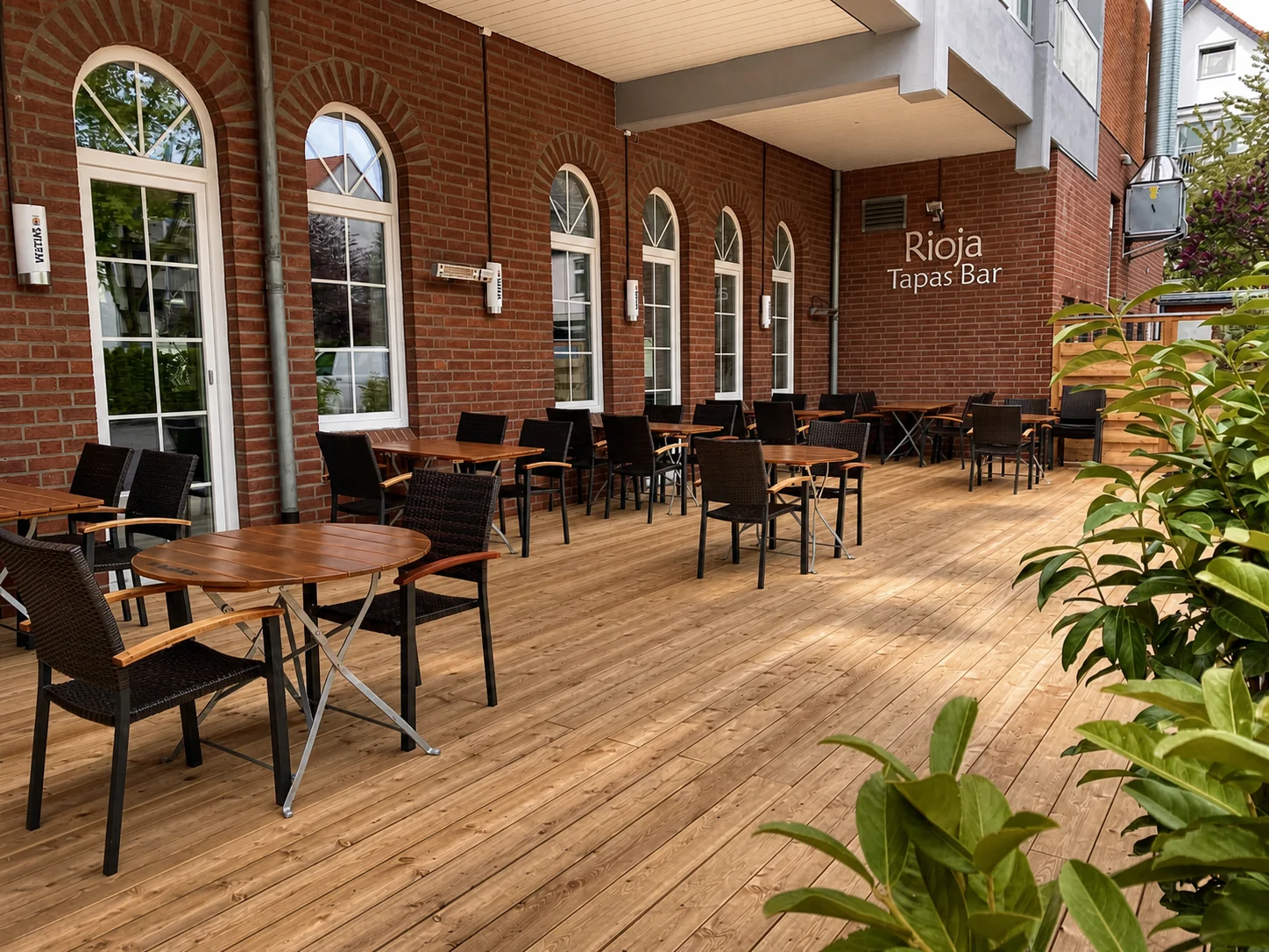 Der überdachte Biergarten des Rioja mit Holztischen, Pflanzen und roter Backsteinfassade